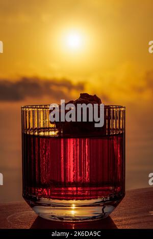 Classico cocktail Negroni bevanda alcolica in vetro retrò cristallo contro luminoso tramonto arancione. Foto Stock