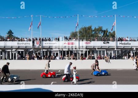 I genitori e i loro figli spingono le loro auto a pedali Austin J40 all'inizio della gara di Settrington Cup per bambini, BARC Revival Meeting, Goodwood, UK Foto Stock