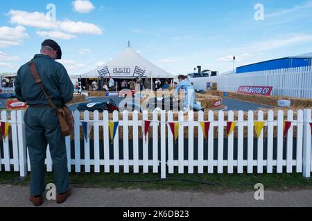 Un uomo in tuta verde di fronte al piccolo circuito per le auto a pedale Austin J40, BARC Revival Meeting, Goodwood circuito automobilistico, Chichester, UK Foto Stock