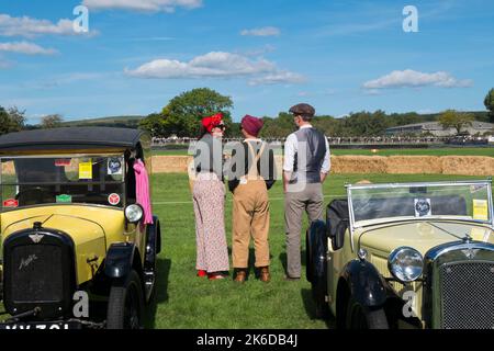 Tre persone vestite d'epoca accanto a due auto Austin 7, una mostra per celebrare il centenario della macchina Austin, Goodwood's Revival Meeting, Regno Unito Foto Stock