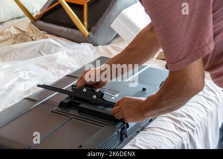 Un uomo messicano che installa la base a muro per il televisore Foto Stock