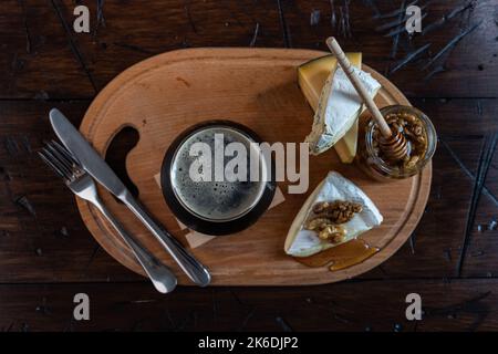 Un bicchiere di birra nera schiumosa e formaggio con miele. Formaggio, miele e birra sul tavolo. Vista dall'alto. Composizione della birra. Foto Stock