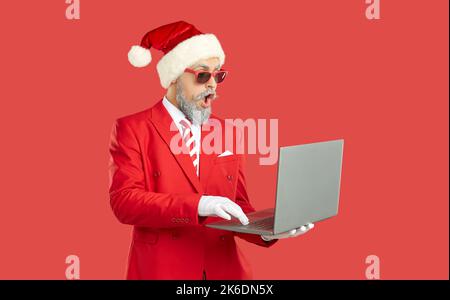 Il giovane Babbo Natale, elegante, moderno e creativo, è stupito da molte e-mail sul suo laptop. Foto Stock