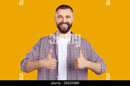Felice giovane uomo in abiti casual sorridendo e mostrando i pollici con entrambe le mani Foto Stock