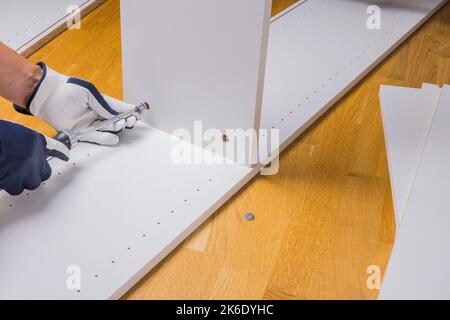 Vista delle mani maschili che assemblano mobili da ufficio bianchi sul pavimento in parquet dell'appartamento. Svezia. Foto Stock