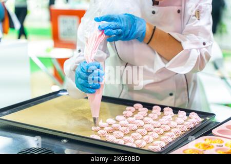 Chiudi le mani dello chef con crema al sacco di pasticceria alla carta pergamena in cucina pasticceria. Foto di alta qualità Foto Stock