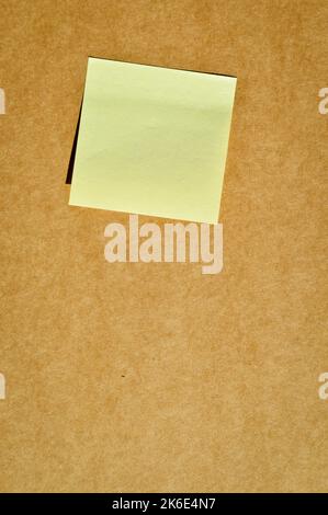 Carta per appunti gialla adesiva quadrata su carta di cartone beige e marrone Foto Stock