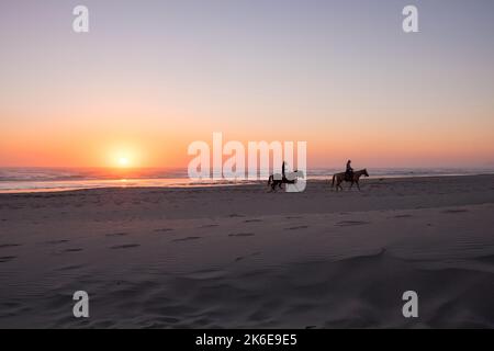 Nehalem Bay, Oregon, USA, due donne che cavalcano cavalli sulla spiaggia al tramonto, Pacific Coast Foto Stock