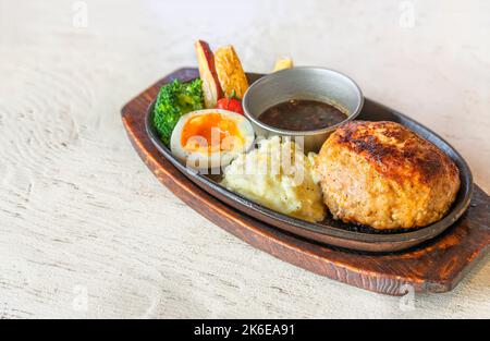 Piastra calda ovale rivestita in smalto opaco di seta nera su un piatto di servizio in legno con un hamburger alla griglia a pezzetti assortito con un uovo sodo, una pezzata di p Foto Stock
