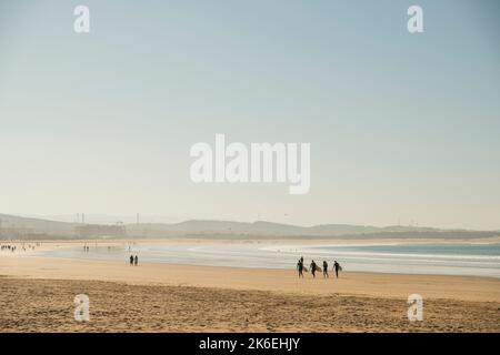 Quattro surfisti trasportano tavole da surf lungo la spiaggia di sabbia dorata di Essaouira nella baia di Mogador, Marocco, Nord Africa Foto Stock
