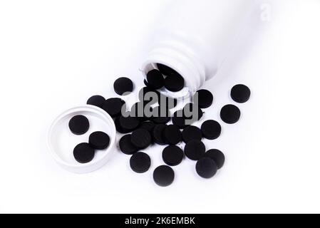 Pillole mediche bianche arancioni nere fuoriescono da un vaso bianco su un isolato su sfondo bianco Foto Stock