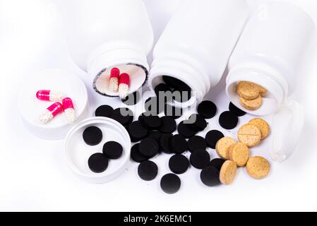 Pillole mediche bianche arancioni nere fuoriescono da un vaso bianco su un isolato su sfondo bianco Foto Stock