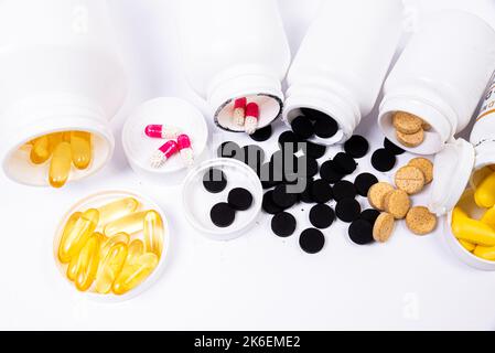 Pillole mediche bianche arancioni nere fuoriescono da un vaso bianco su un isolato su sfondo bianco Foto Stock