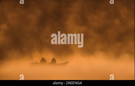 Una barca unica con due pescatori su un lago nebbioso durante l'alba, minimalismo, spazio copia, orizzontale Foto Stock