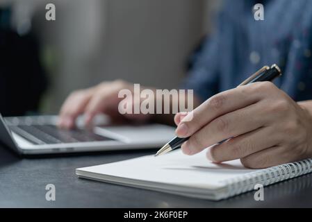 scrittura a mano maschile in notebook con penna su computer portatile in ufficio moderno. Foto Stock