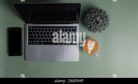 Computer portatile e fiore smartphone caffè tazza su sfondo verde.Top vista copia spazio vuoto. Foto Stock