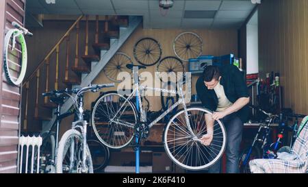 Meccanico esperto in abiti casual è impegnato a controllare il manubrio e la ruota anteriore della bicicletta, quindi a regolarlo e fissarlo con attrezzi. Riparazione dei cicli e del concetto di persone. Foto Stock