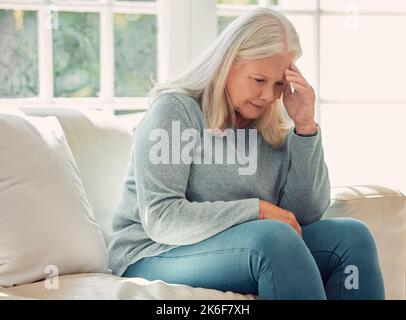 È giusto imparare da ogni esperienza. una donna anziana che ha un mal di testa sul divano a casa. Foto Stock