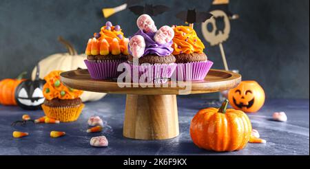 Stand con gustosi cupcake di Halloween, caramelle e zucche su sfondo grunge Foto Stock