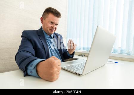 Un uomo d'affari frustrato mostra la sua frustrazione mentre lavora sul suo notebook. un dipendente arrabbiato è furioso di fronte a un computer non funzionante. Foto Stock