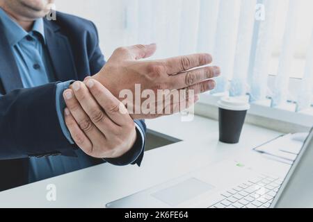 primo piano il massaggio dell'uomo dell'impiegato sulla sua mano e braccio per il dolore di rilievo dal lavoro duro, concetto della sindrome del tunnel carpale Foto Stock