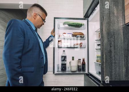 Uomo alla ricerca di cibo in un frigorifero aperto in cucina a tarda notte. L'uomo sembra un bachelor affamato. Foto Stock