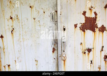 La vecchia porta dell'edificio. Porta in metallo verniciato con macchie di ruggine e graffi, ingresso al territorio in cattive condizioni Foto Stock