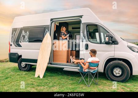 Donna che asciuga pa in camper van mentre l'uomo gioca ukulele all'aperto Foto Stock