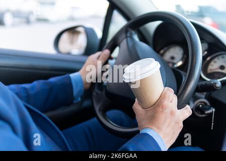 Uomo conducente con mano take away andare caffè tazza durante la guida di un'auto al mattino, primo piano, stile di vita della gente, vacanza estiva viaggio concetto. pericolo Foto Stock