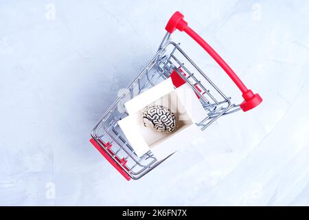 Cervello umano in una scatola di spedizione posta in un carrello della spesa in miniatura isolato su grigio, vista dall'alto. Il concetto di acquisto di un nuovo cervello. Foto Stock