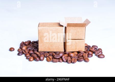 Scatole di cartone in miniatura e chicchi di caffè tostati isolati su sfondo neutro. Concetto di produzione e fornitura di caffè. Foto Stock