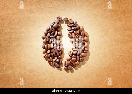 Simbolo del chicco di caffè ottenuto da chicchi di caffè tostati disposti su uno sfondo di carta artigianale. Foto Stock