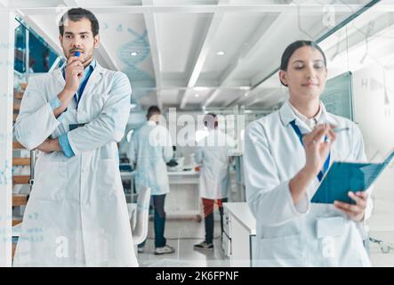 Porre domande e indagare sulle risposte. due giovani scienziati che si occupano di brainstorming con note su uno schermo di vetro in un laboratorio. Foto Stock