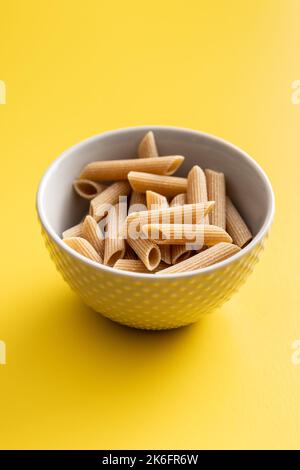 La pasta a grani interi crudi. Penne crude in ciotola su fondo giallo. Foto Stock