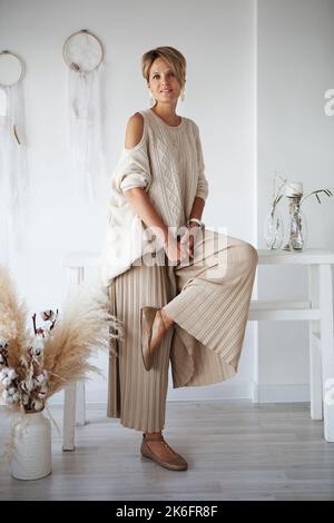 Bella donna interior designer decorare una nuova casa, seduta in un maglione beige e pantaloni Foto Stock