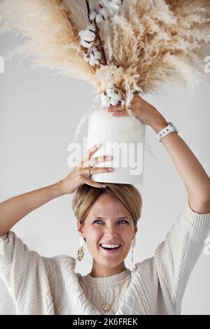 Bel designer d'interni decorare la nuova casa con un bouquet di cotone e erba secca. Donna felice e ridendo, avendo divertimento feeling, godere di posizioni Foto Stock