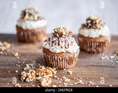 Gustoso muffin al cioccolato con mascarpone cremoso e cioccolato in cima, ricoperto di noci. Collocato su una scrivania in legno. Cupcake dolce fresco e fatto in casa. Foto Stock