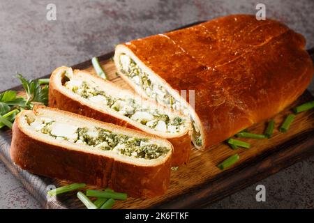 Deliziosa torta fatta in casa farcita con uova sode, cipolle verdi, prezzemolo, aneto e spinaci primo piano su un asse di legno sul tavolo. Orizzontale Foto Stock