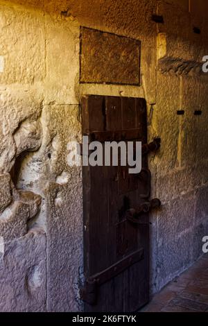 Cella di Dungeon ha bloccato la vecchia porta di legno intorno ad un muro di pietra. Foto Stock