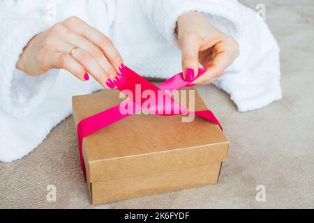 Donna imballaggio scatola sorpresa con nastro rosso. Confezione regalo decorata. Festa di Natale. Sorpresa di compleanno. Regalo fatto a mano. Artigianato presente Foto Stock