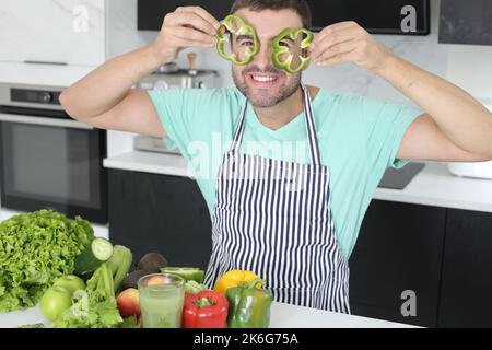 Uomo che gioca con peperoni verdi in cucina Foto Stock