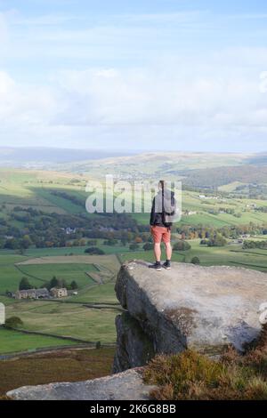 Earl Crag, North Yorkshire, Regno Unito. Uomo in piedi sullo sperone roccioso che si affaccia sul panorama. Foto Stock