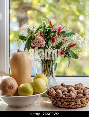 Composizione autunnale, bouquet di fiori in vaso, zucca di butterno, mele e noci Foto Stock