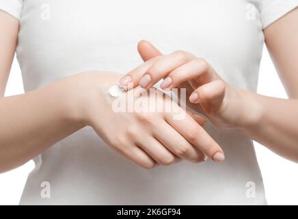 Foto ritagliata di una donna in t-shirt bianca applicando crema per le mani, isolata sul bianco. Unghie naturali corte e ben curate. Foto Stock