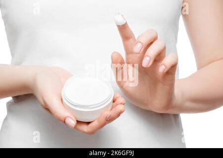 Primo piano scatto di una donna in t-shirt bianca con un vasetto di crema per le mani, isolato su bianco. Unghie naturali corte. Foto Stock