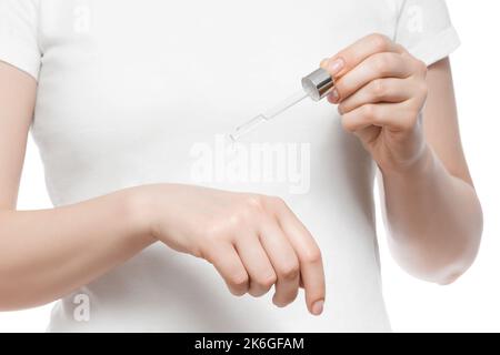 Colpo corto di una donna in T-shirt bianca con pipetta e siero, isolato su bianco. Belle unghie corte naturali. Foto Stock