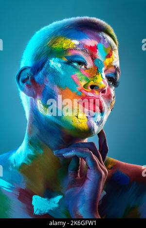 Dai un'occhiata più da vicino e scoprirai tutte le moltitudini. Studio shot di una giovane donna che posa con vernice multicolore sul suo viso. Foto Stock