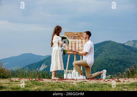 Offerta in montagna. Un ragazzo mette un anello sulla sua sposa mentre si alza sul ginocchio. Coppia felice. Sposami. Buona fortuna con la proposta. Foto Stock
