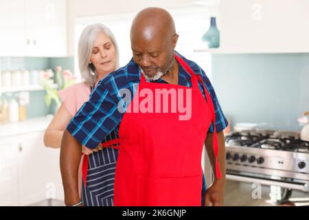 Felice coppia anziana diversa indossando grembiuli in cucina Foto Stock