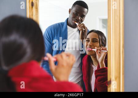 Felice coppia diversa nel spazzolare i denti in bagno, guardando in specchio sorridente Foto Stock